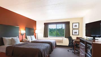 A hotel room with two beds, a desk, a chair, a TV, and a window with a view of trees.