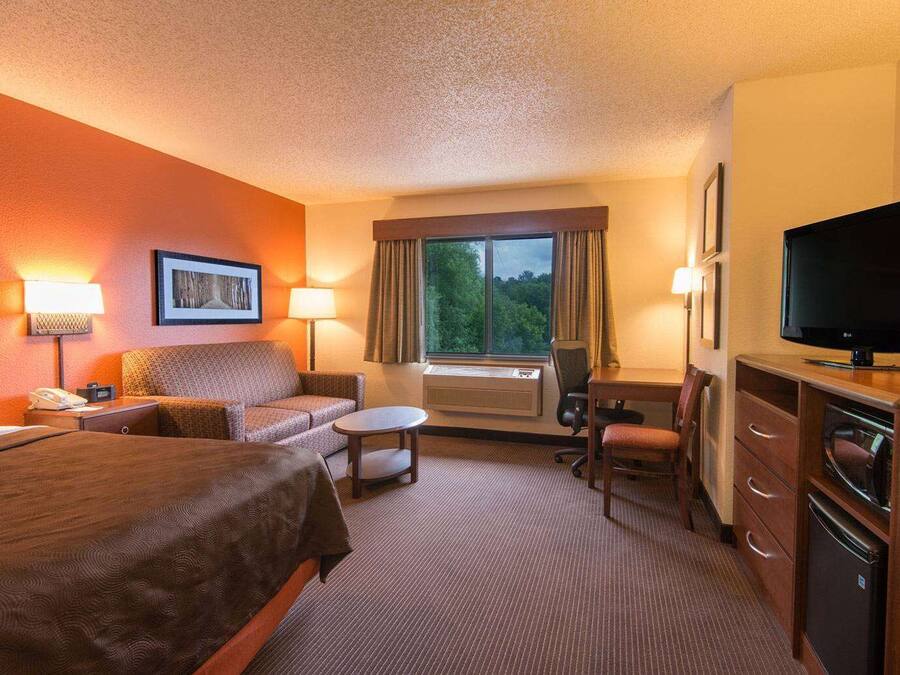 Et hotelværelse med seng, sofa, skrivebord, stol, fjernsyn og et vindue med gardiner.