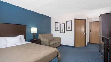 Habitación de hotel con una cama grande, una silla, un escritorio con lámpara, cuadros en la pared y un armario.