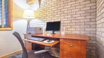 Un bureau en bois avec un ordinateur, une lampe et une chaise, dans une pièce aux murs en briques.