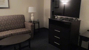 A hotel room with a sofa, a small table, a lamp, a TV on a cabinet, and a carpeted floor.