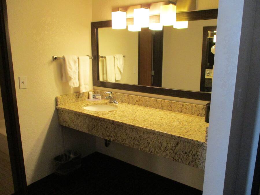 Une salle de bain avec un lavabo doté d’un plan de travail en granit, un miroir et un porte-serviettes.
