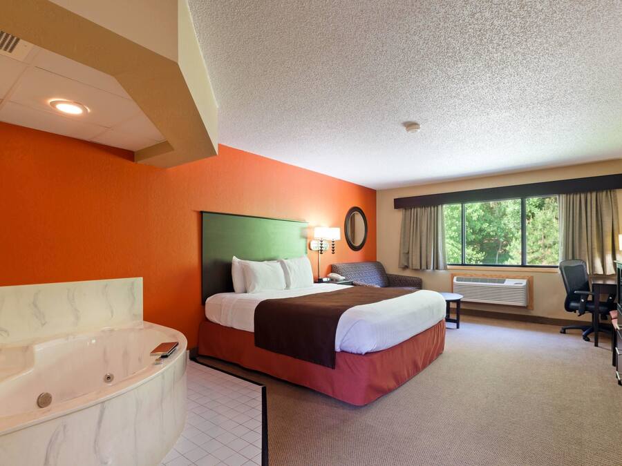 Ein Hotelzimmer mit einem großen Bett, einem separaten Badezimmer mit Whirlpool, einem Schreibtisch und einem Fenster mit Vorhängen.