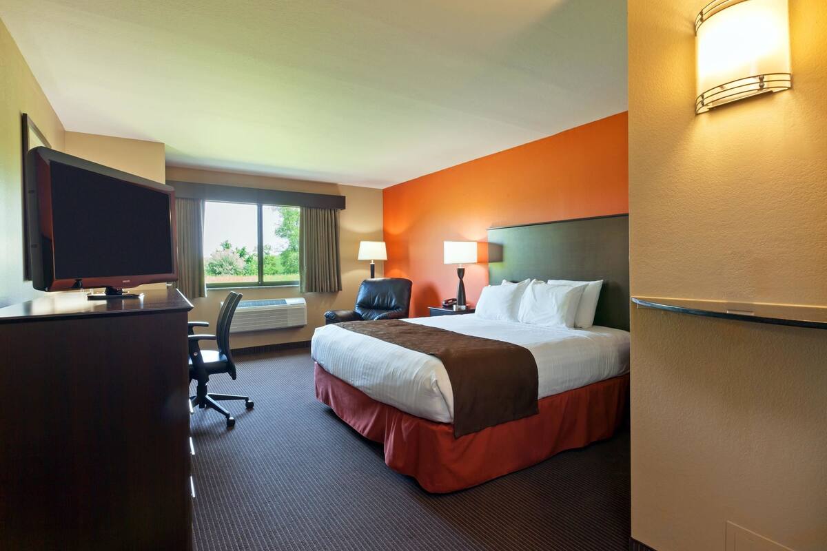 A hotel room with a bed, desk, chair, TV, and two lamps.