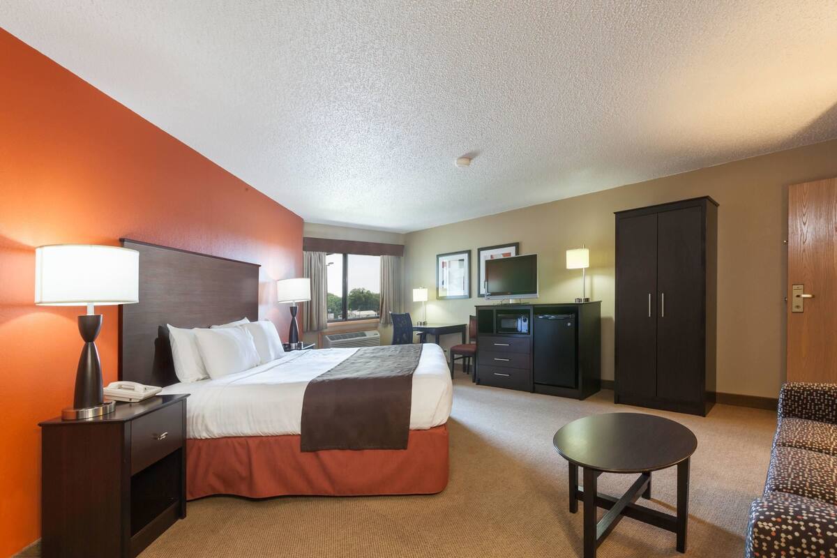 A hotel room with a bed, bedside table, lamp, desk, TV, wardrobe, and a small round table.