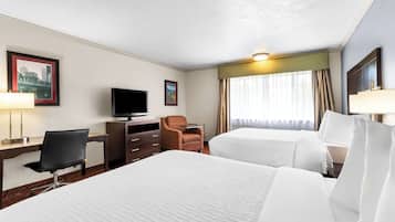 A hotel room with two beds, a desk with a chair, a television, and a window with curtains.