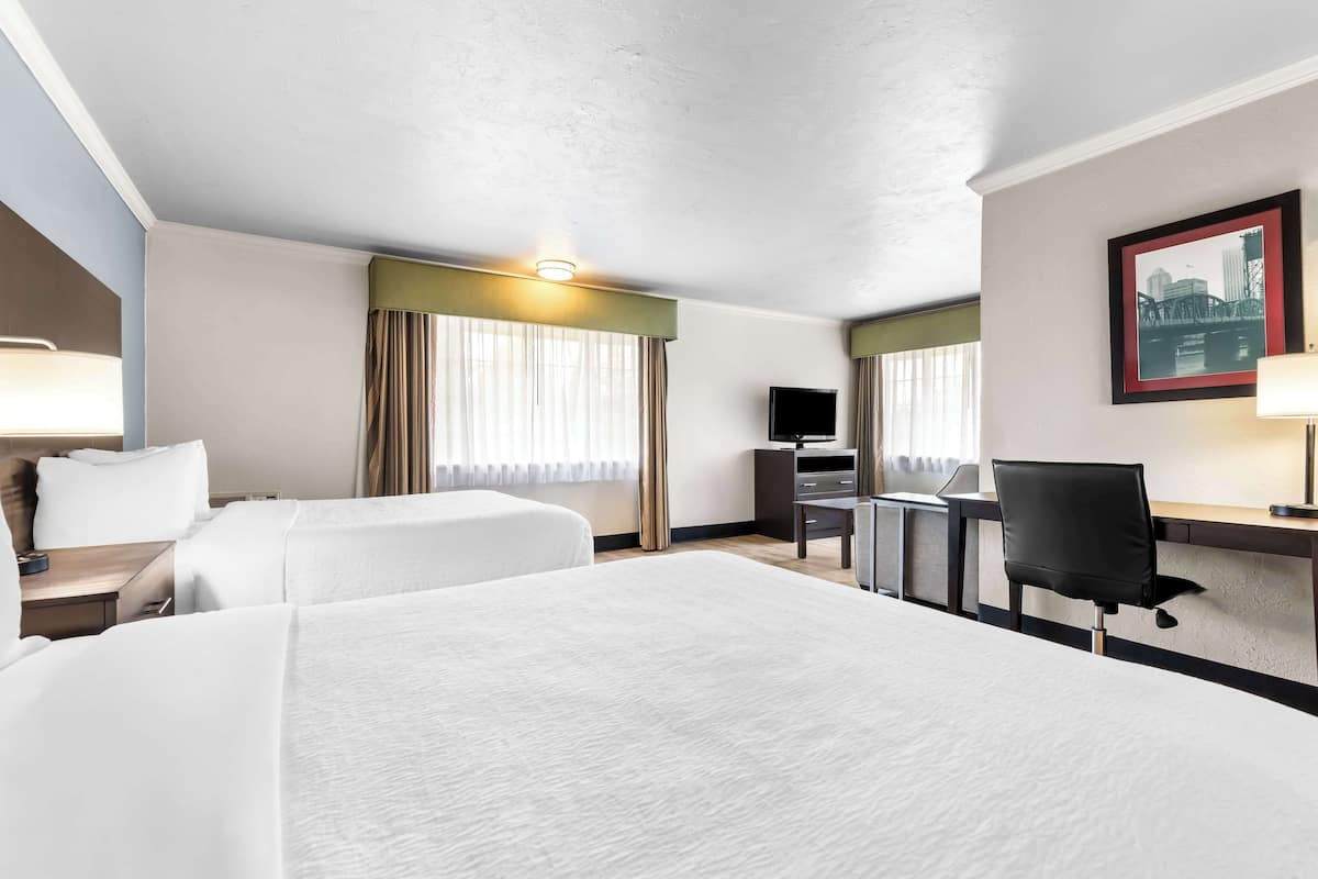 A hotel room with two beds, a desk, a chair, a TV, and a framed picture on the wall.