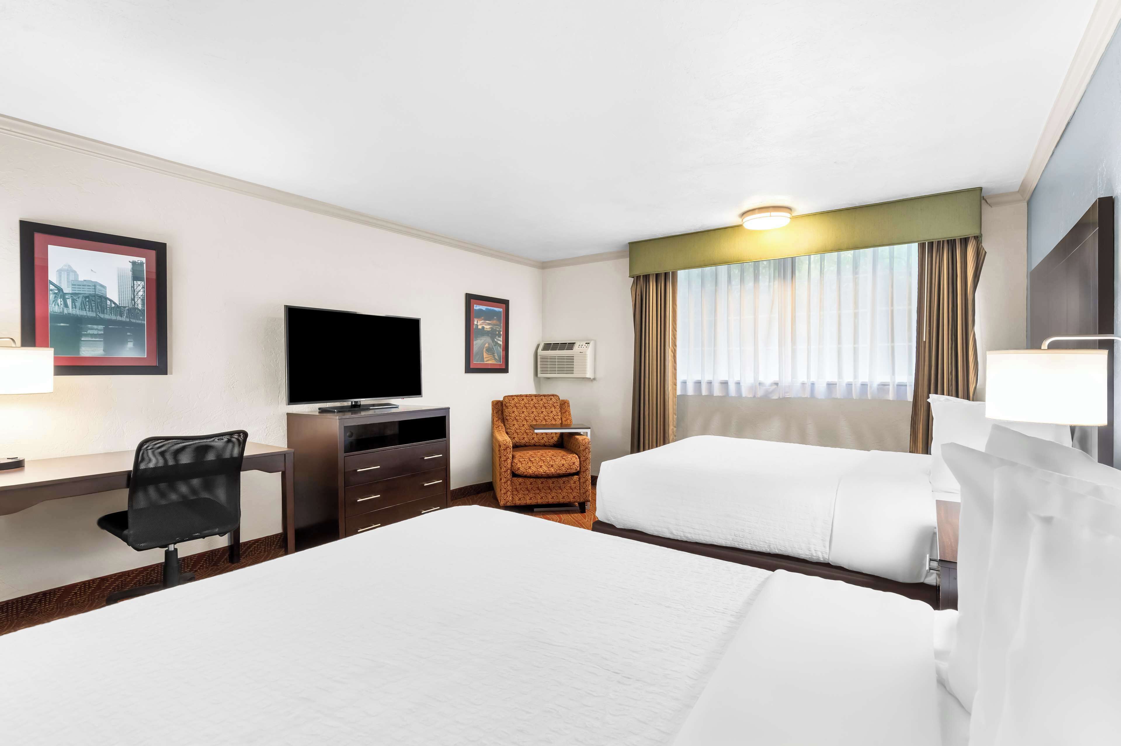 A hotel room with two beds, a desk with a chair, a television, and a window with curtains.
