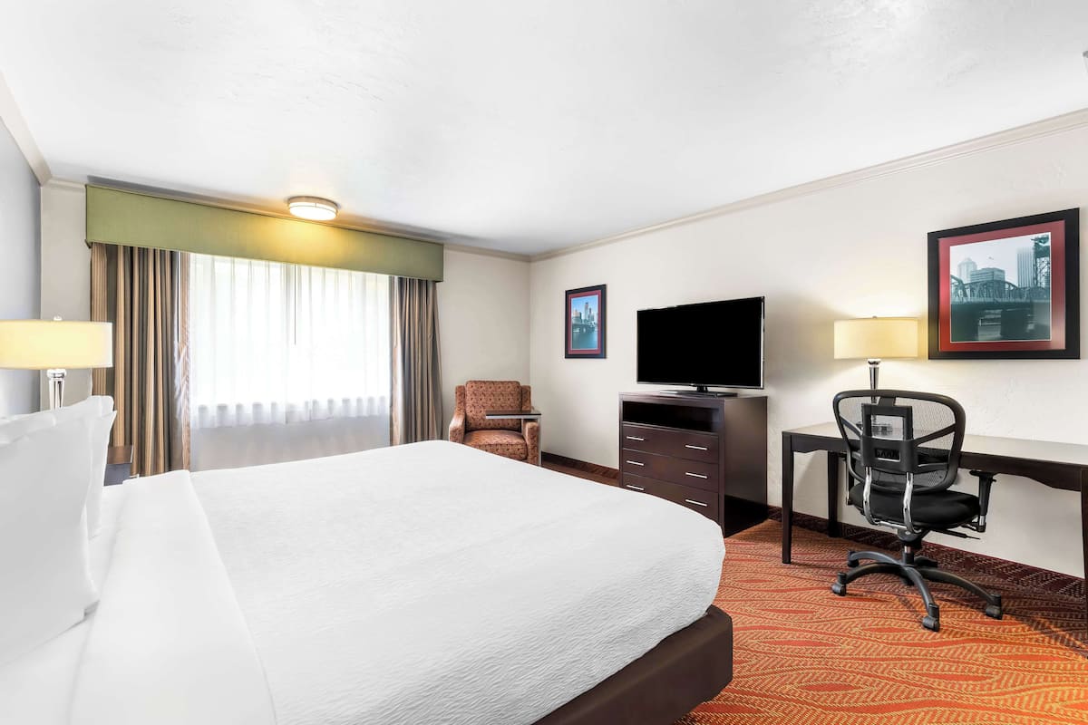 A hotel room with a large bed, a desk with a chair, a television, and a window with curtains.