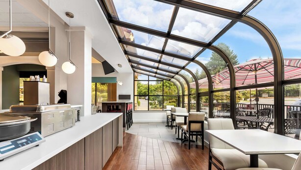 A restaurant with a modern interior, featuring a kitchen area with stainless steel appliances, a counter with a digital scale, and seating with tables and chairs. - Best Western Plus Parkway Inn (Wilsonville)