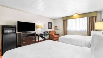 A hotel room with two beds, a television, a desk with a chair, and a window with curtains.