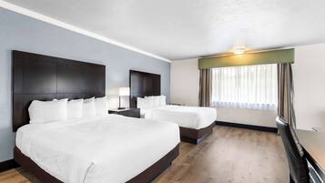 A hotel room with two beds, a desk, a chair, a nightstand, and a window with curtains.