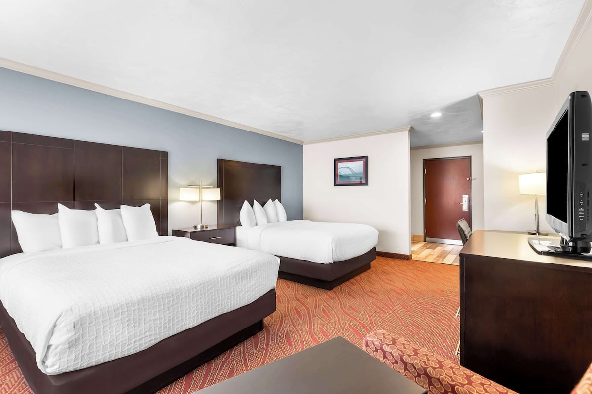 A hotel room with two beds, a desk, a television, and a door leading to a bathroom.