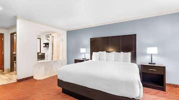 Habitación de hotel con una cama grande, dos mesitas de noche con lámparas, un espejo y un baño visible a través de una puerta abierta.