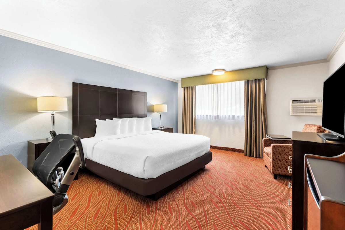 A hotel room with a large bed, two bedside tables with lamps, a desk, a chair, and a television.