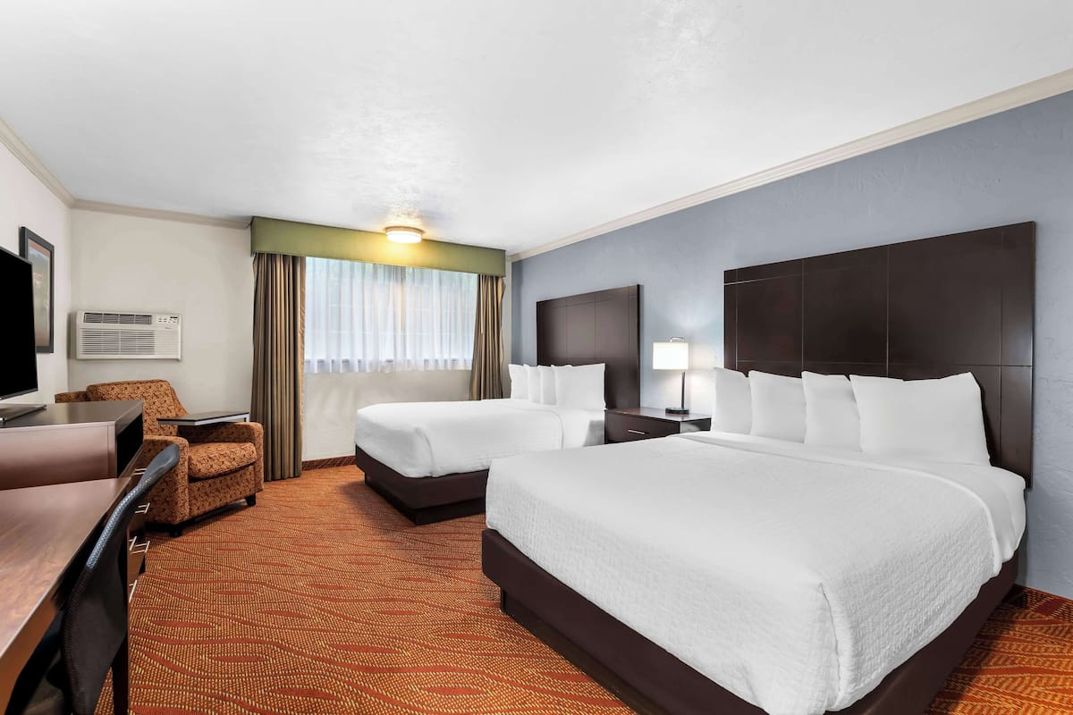 A hotel room with two beds, a desk, a chair, a TV, and a window with curtains.