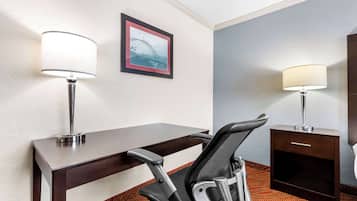 A hotel room with a desk, two lamps, a chair, a framed picture, and a small cabinet.