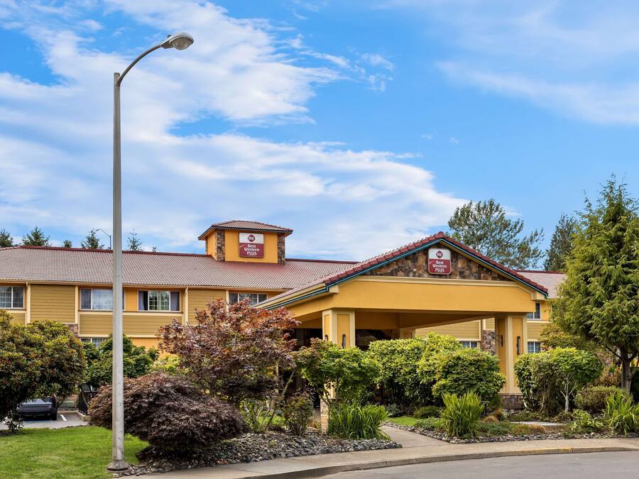 Ein gelbes Gebäude mit rotem Dach, ein Schild, das es als Best Western Hotel kennzeichnet, und ein gepflegter Garten davor.