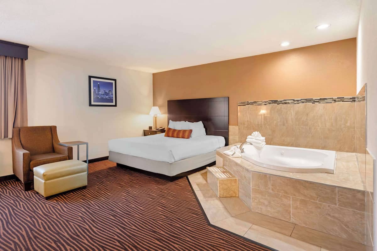 A hotel room with a bed, a chair, a sofa, a bathroom with a bathtub, and a cityscape picture on the wall.