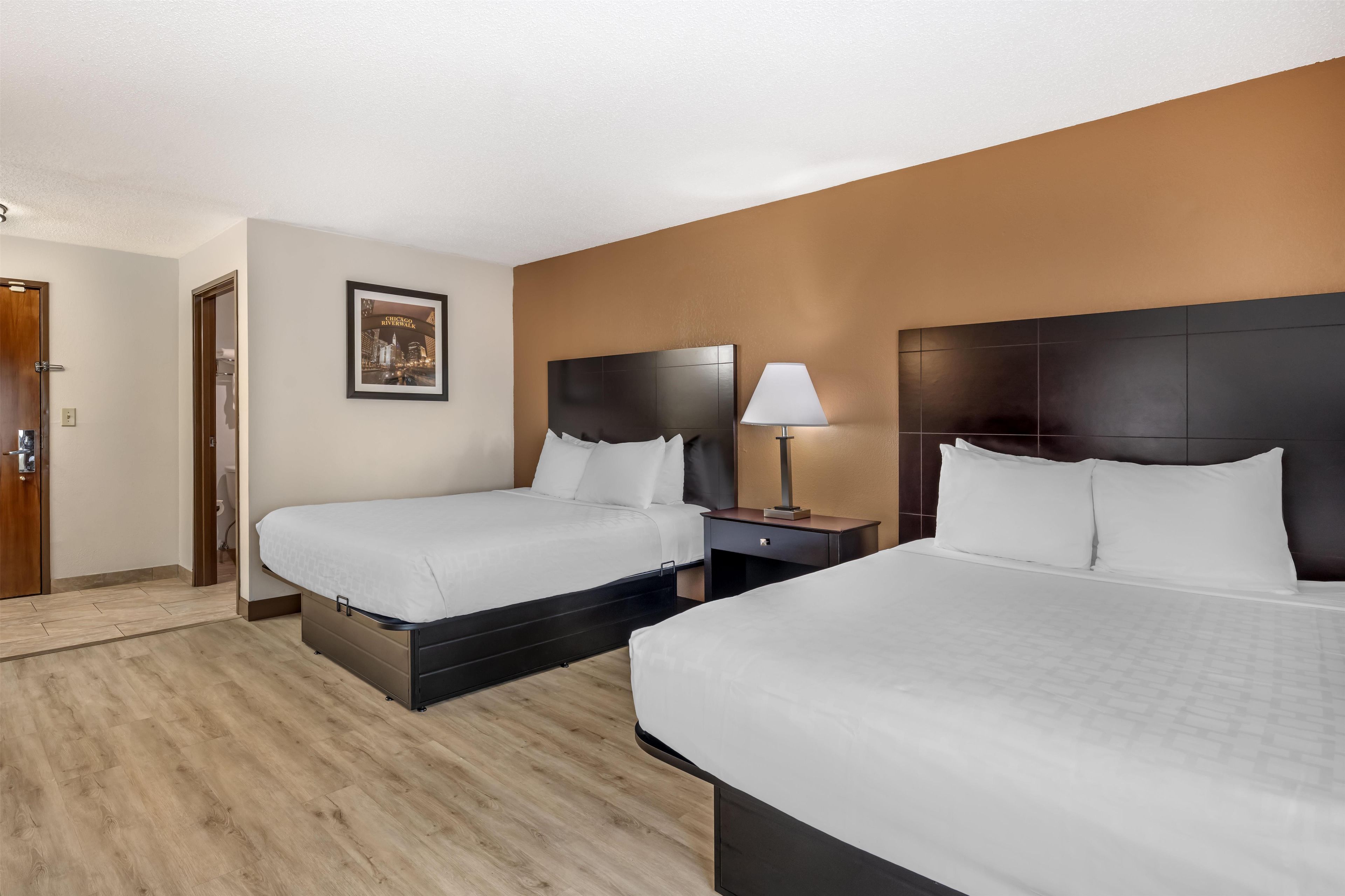 A hotel room with two beds, a nightstand, a lamp, and a framed picture on the wall.