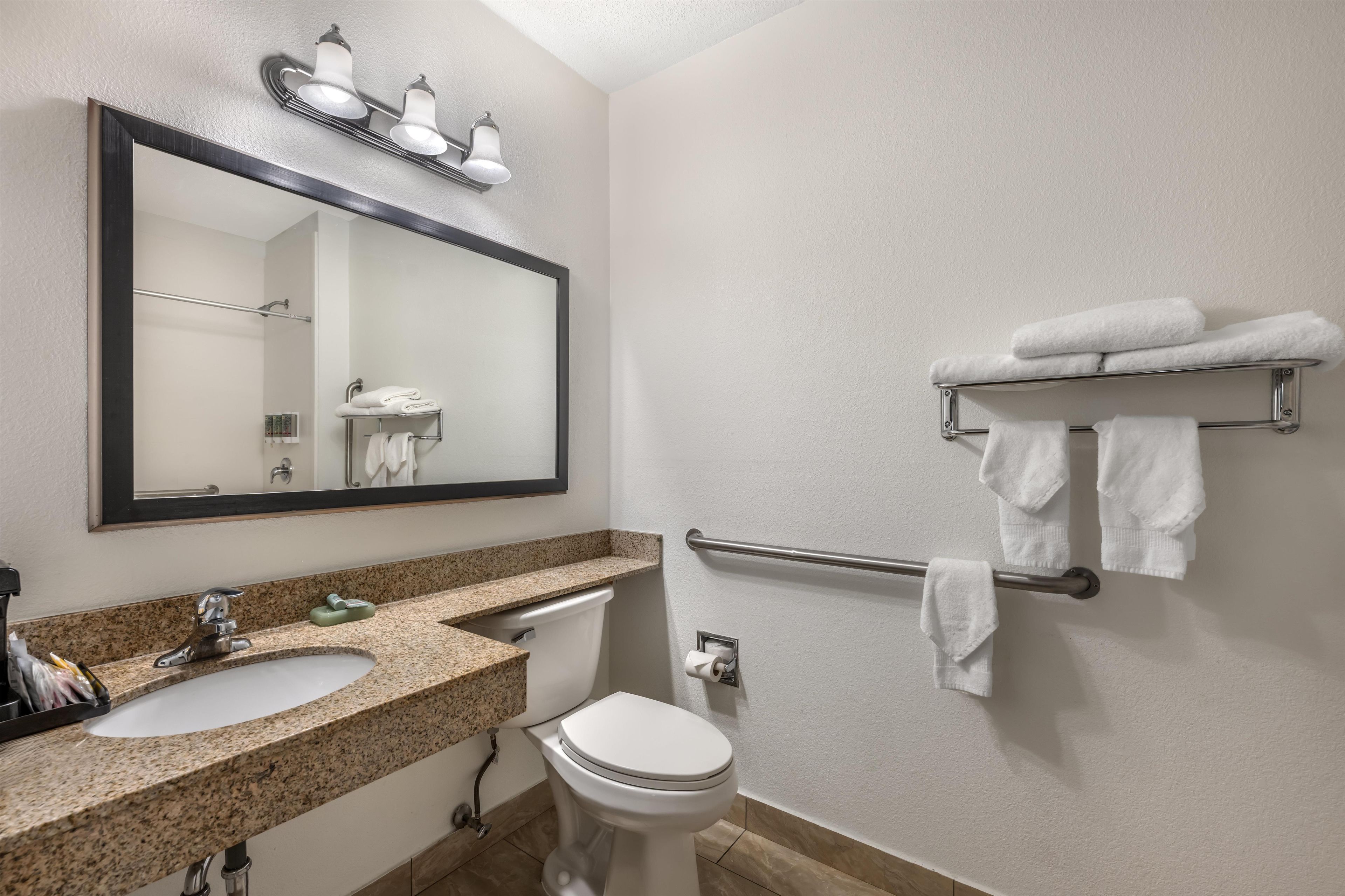 A bathroom with a granite countertop sink, a toilet, a towel rack, and a mirror.