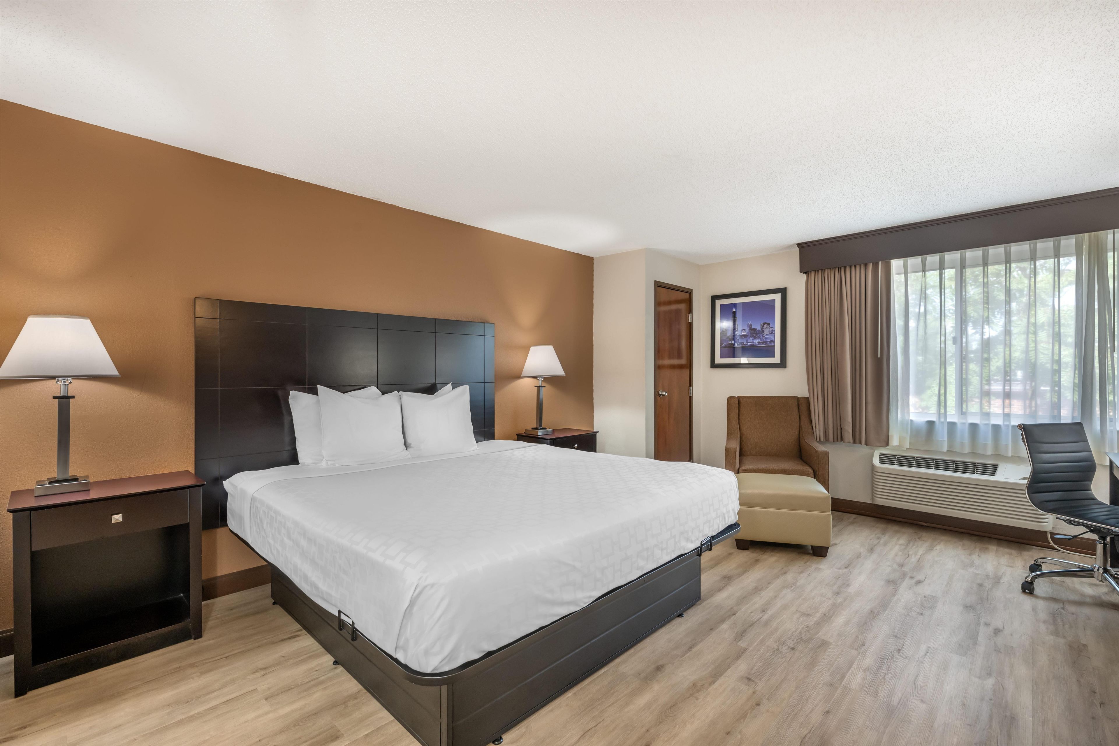 Une chambre d’hôtel avec un grand lit, deux tables de chevet, une chaise, un bureau et une fenêtre avec des rideaux.
