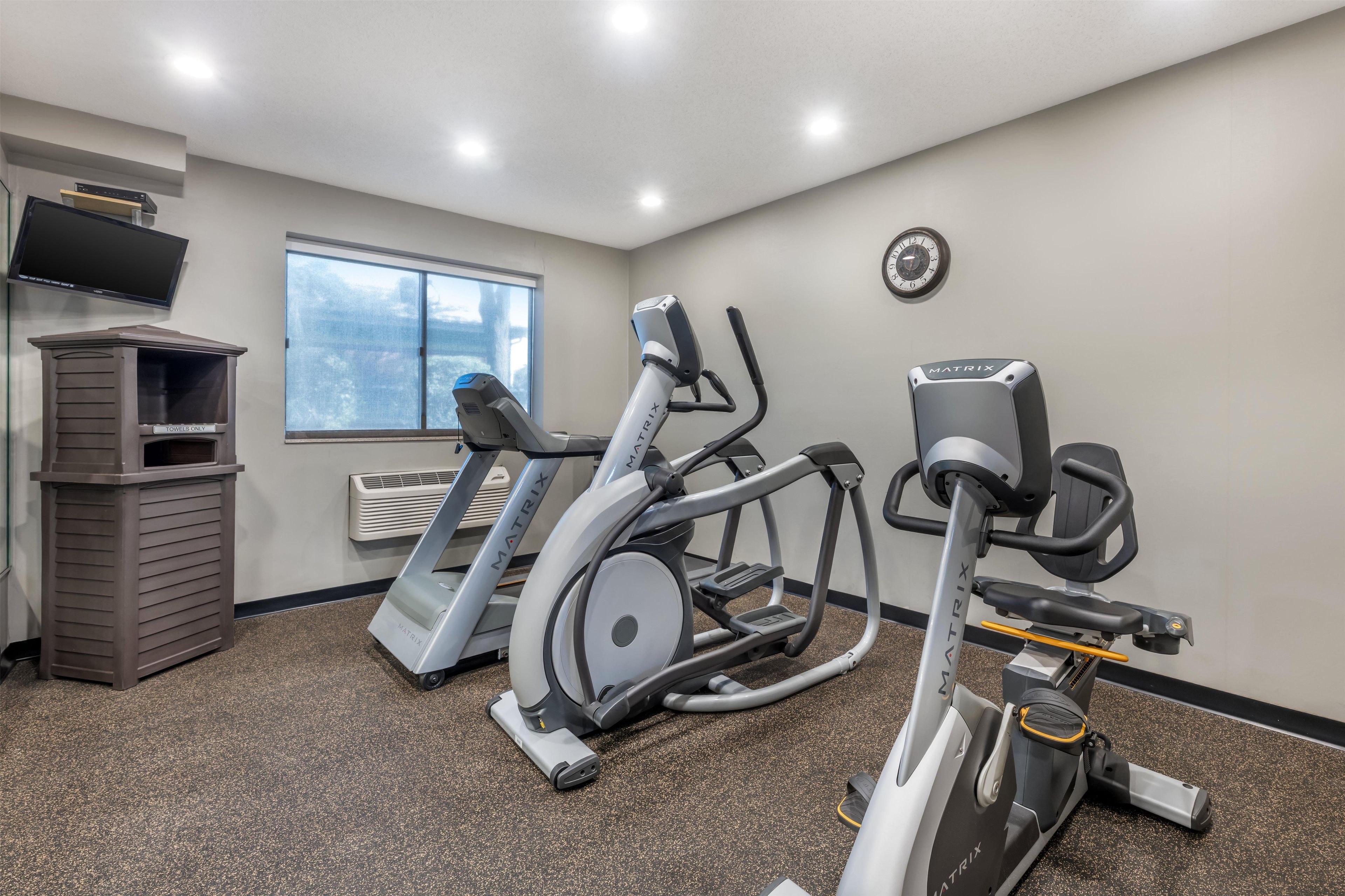 A gym with treadmills, an elliptical, and a stationary bike, a TV, and a clock on the wall.