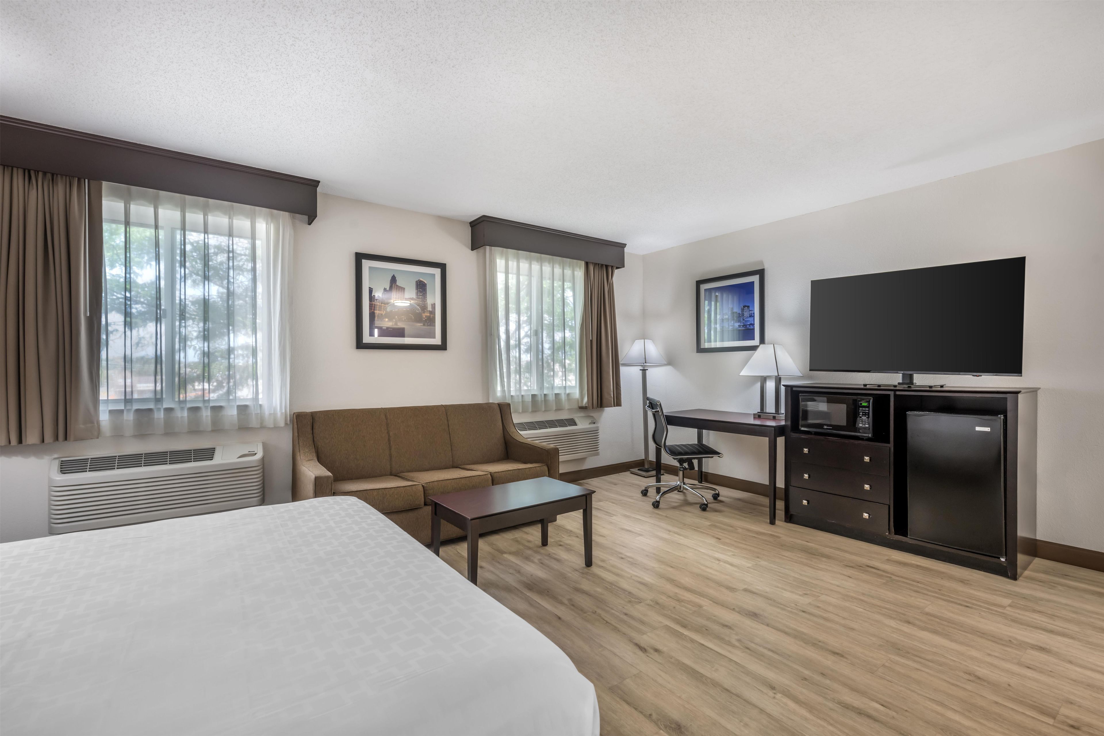 A hotel room with a bed, a sofa, a desk, a chair, a TV, and a microwave.