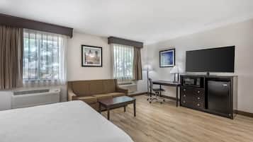 A hotel room with a bed, a sofa, a desk, a chair, a TV, and a microwave.