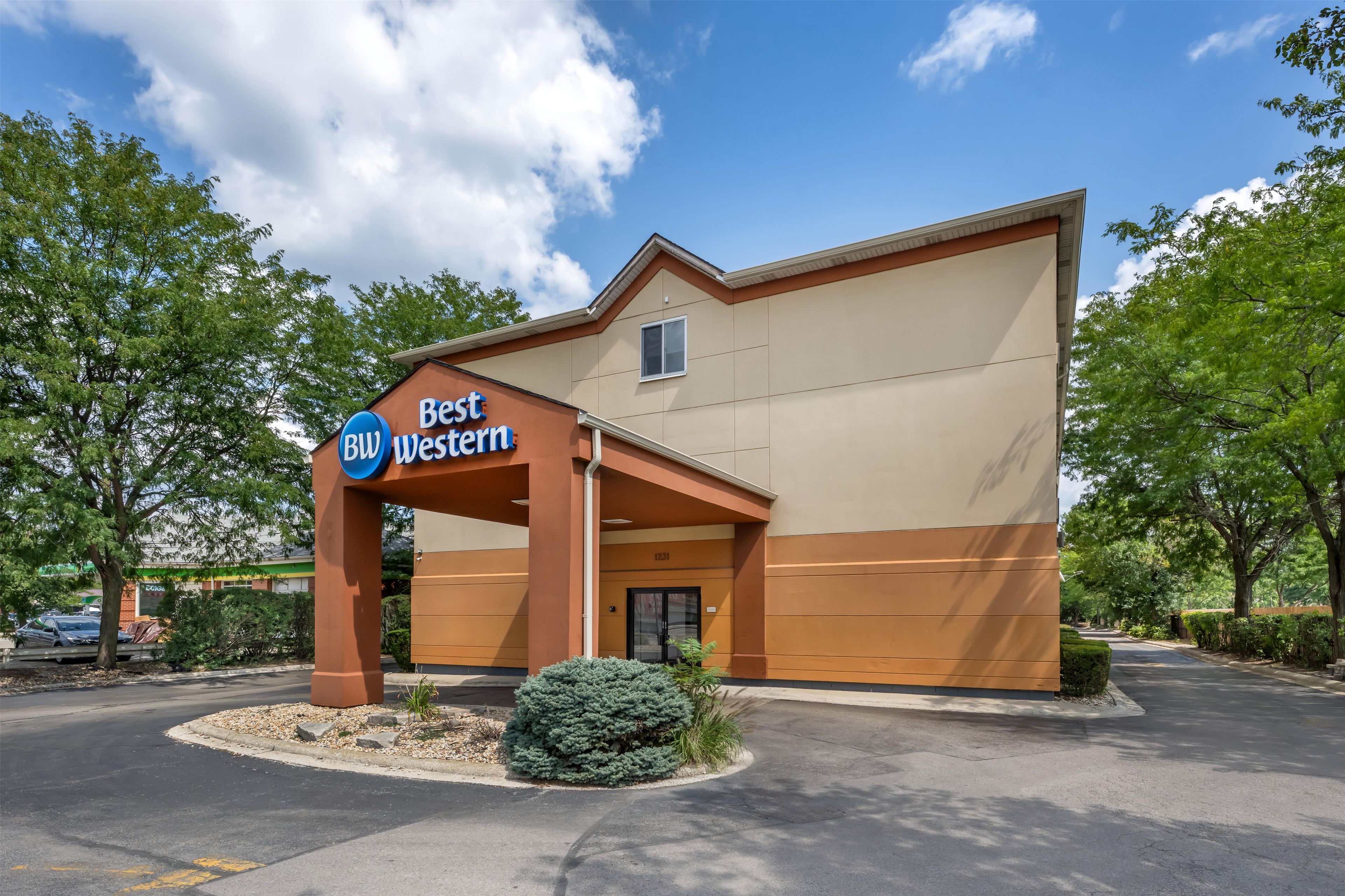 Un hotel Best Western con fachada marrón, cielo despejado y entorno con vegetación.