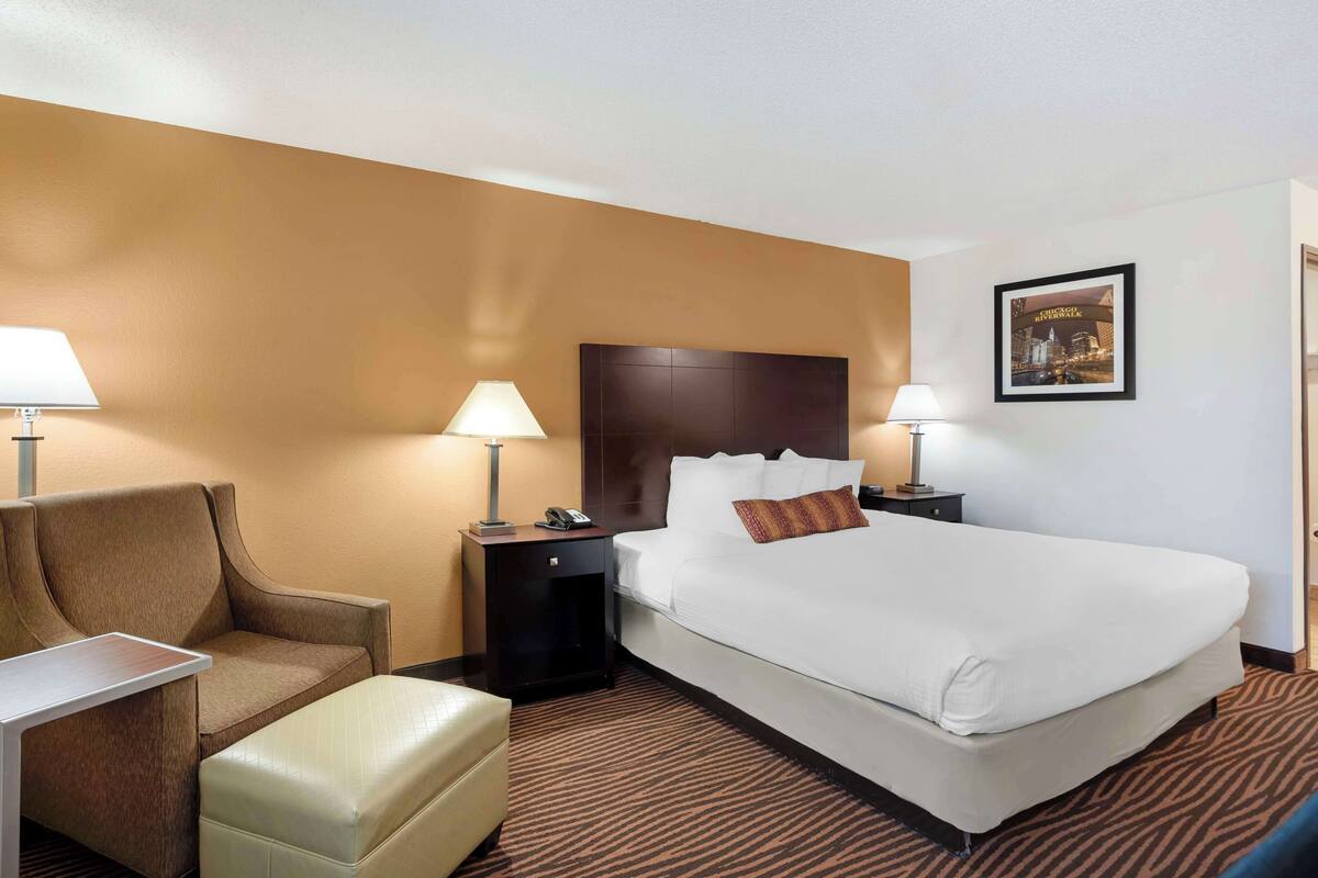 A hotel room with a bed, a chair, a desk, a nightstand, and a lamp.