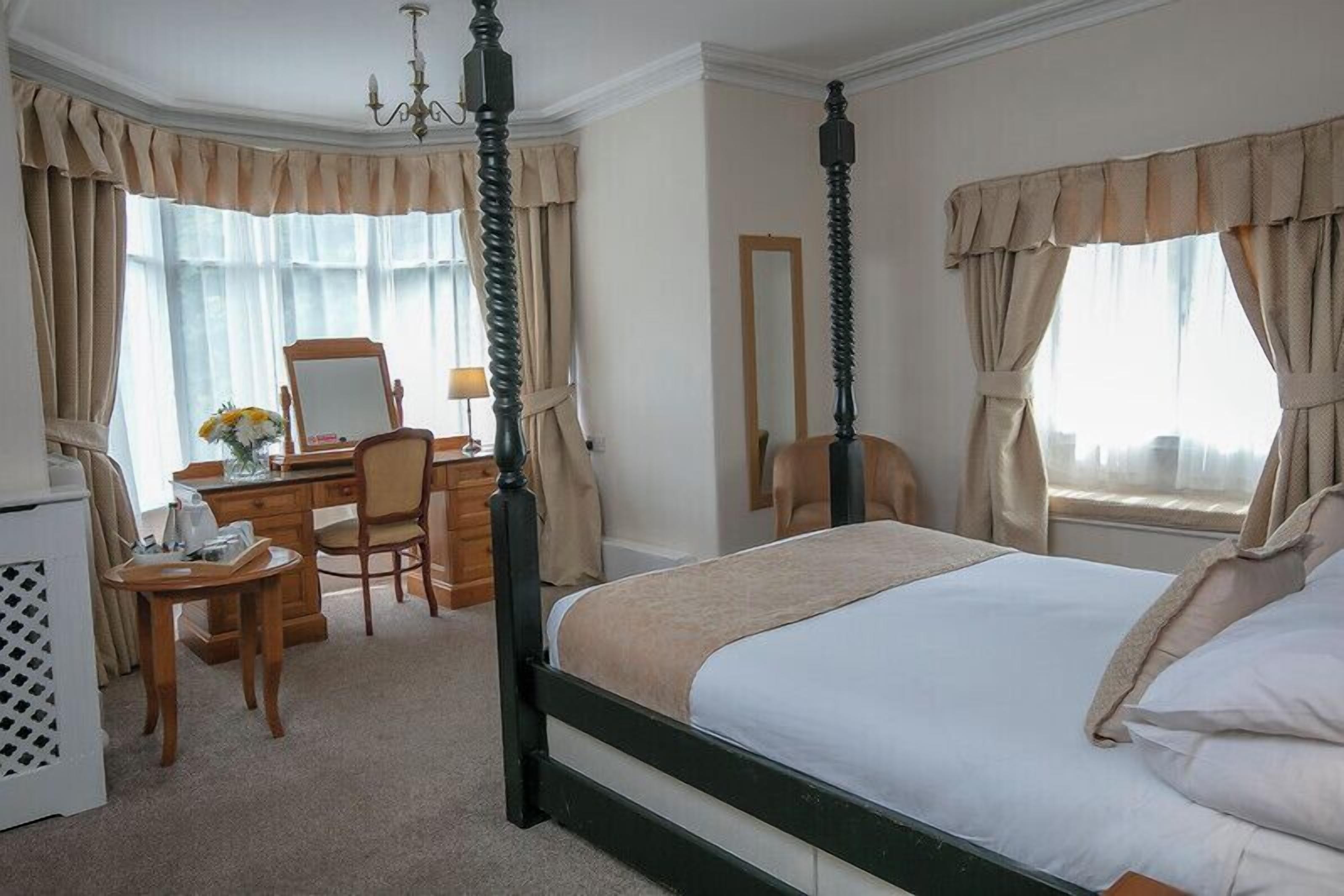 A hotel room with a four-poster bed, a desk with a chair, a mirror, and a dresser.