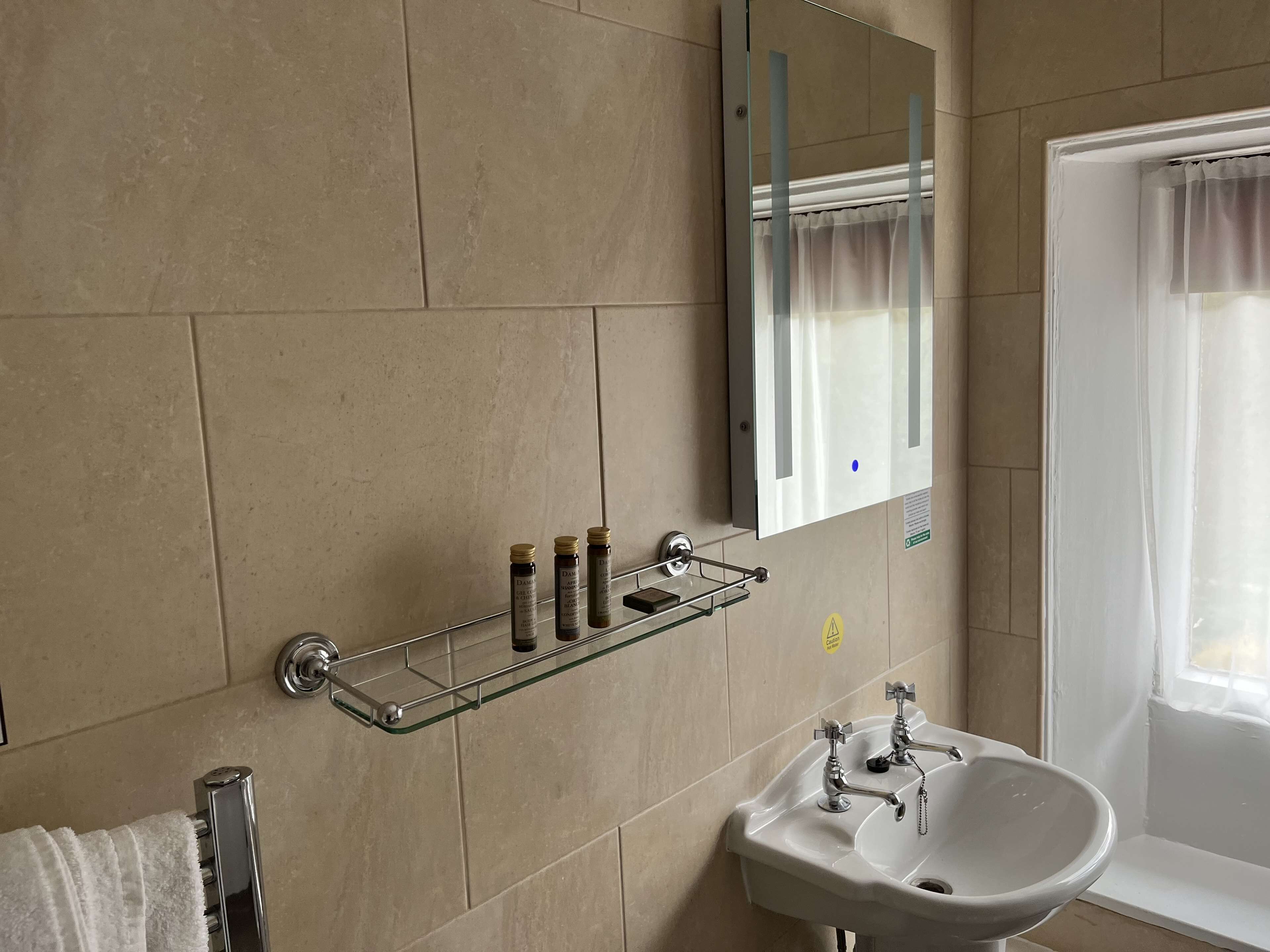 A bathroom with a white sink, a mirror, and a glass shelf with toiletries.