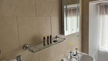 A bathroom with a white sink, a mirror, and a glass shelf with toiletries.