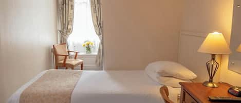 Ein Hotelzimmer mit Bett, Schreibtisch mit Lampe, Stuhl und einem Fenster mit Vorhängen.