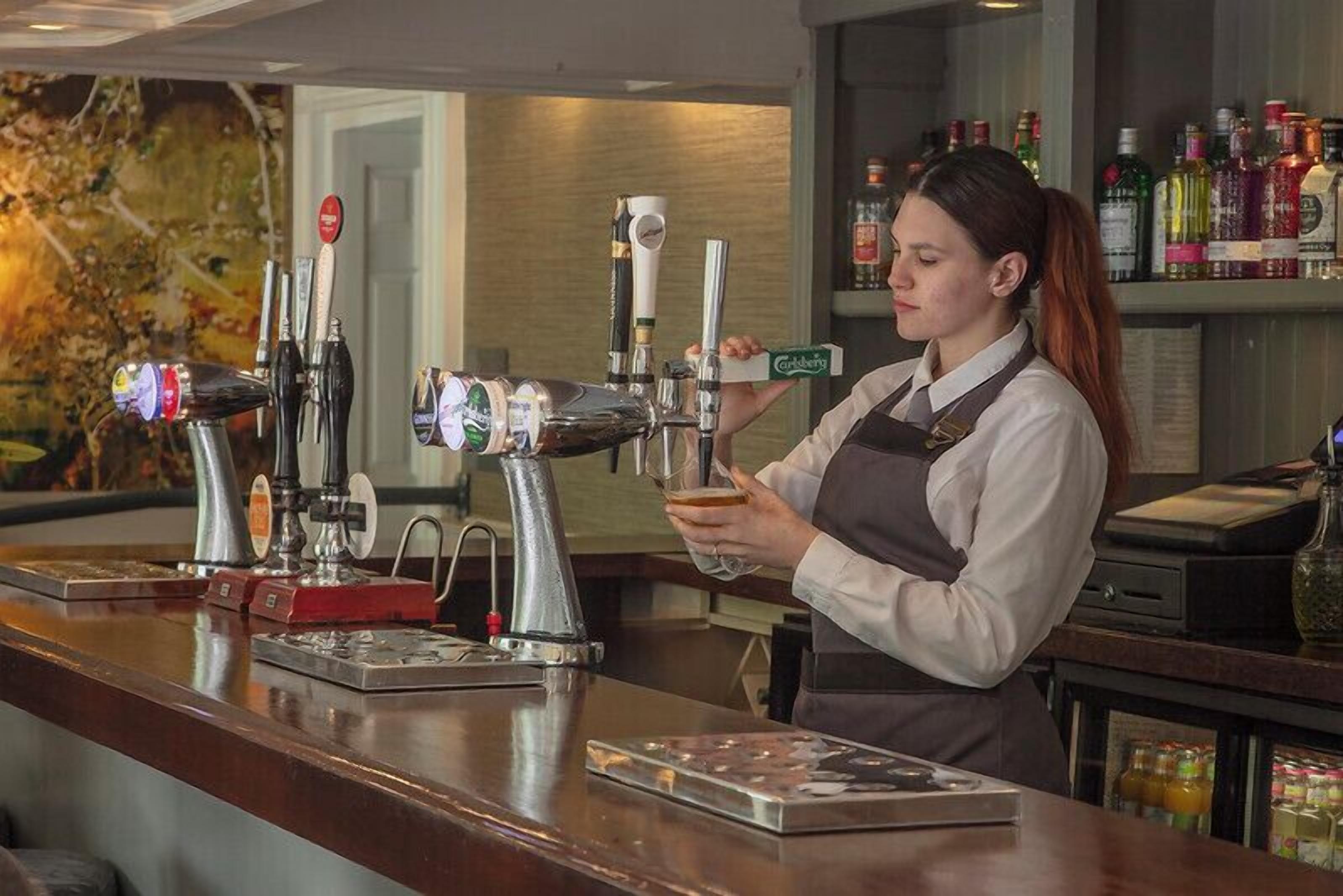 A barista at a bar with multiple beer taps and a variety of liquor bottles in the background.