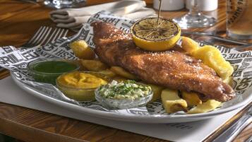 Un plato de pescado frito con patatas y rodajas de limón, acompañado de dos salsas para mojar.
