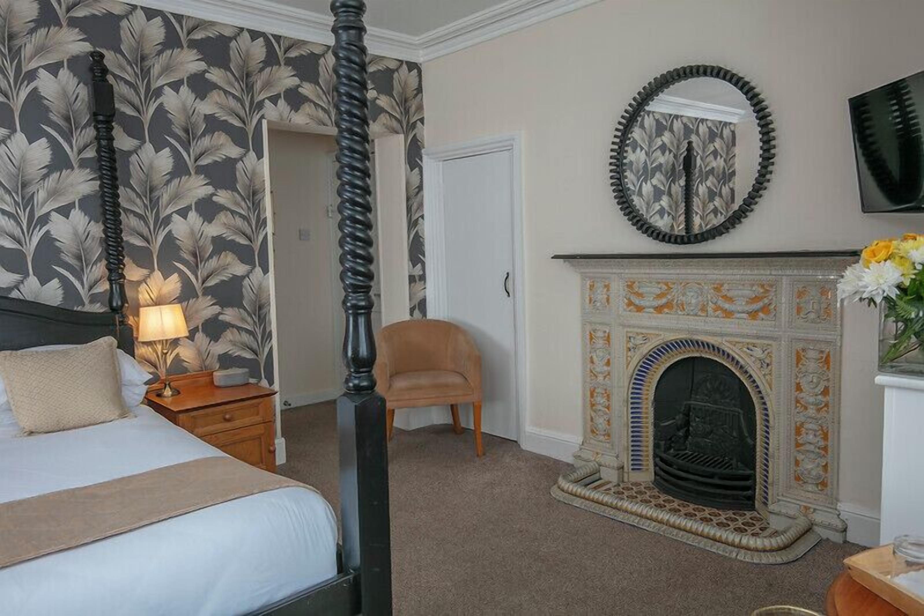 A bedroom with a four-poster bed, a fireplace, and a mirror on the wall.