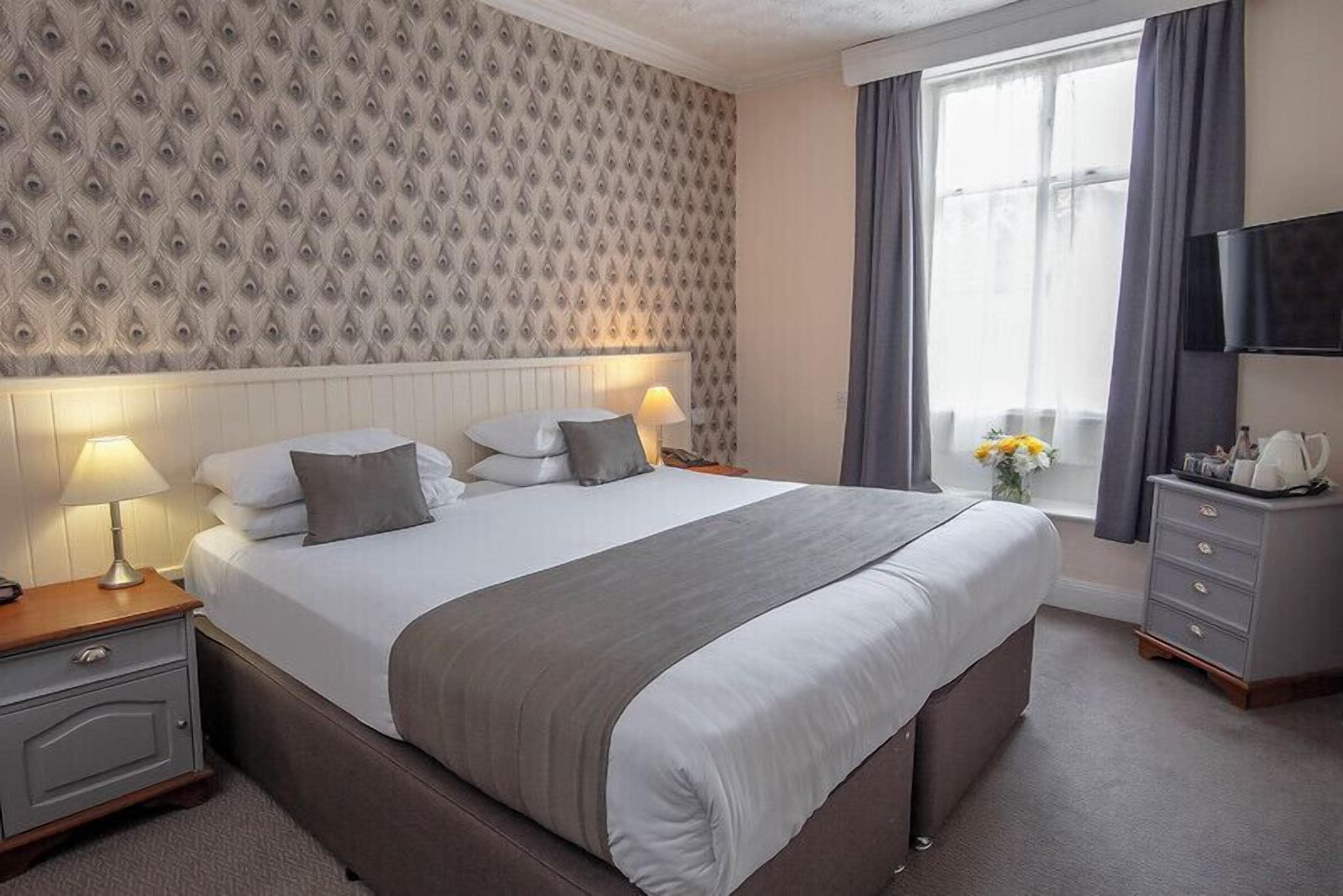 A neatly arranged hotel room with a large bed, bedside lamps, a dresser, and a television on the wall.