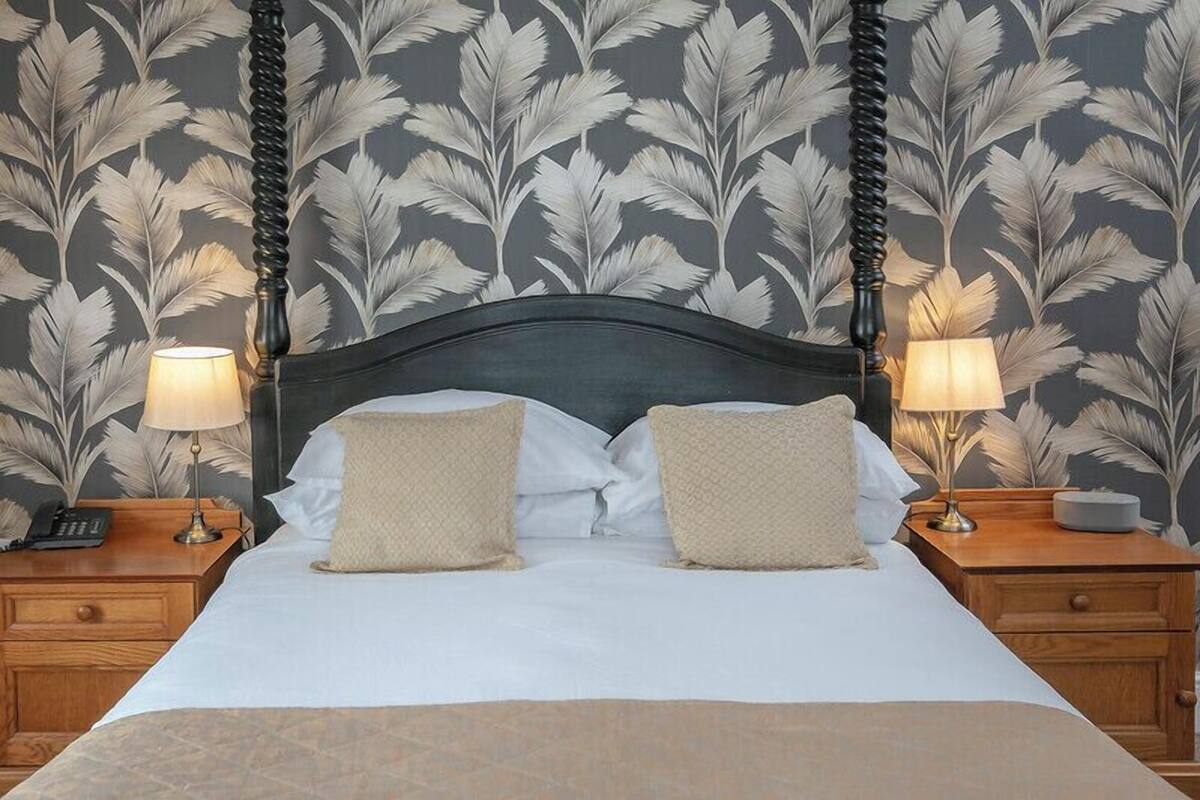 A neatly made bed with a dark headboard, two bedside lamps, and a nightstand with a telephone and a lamp.