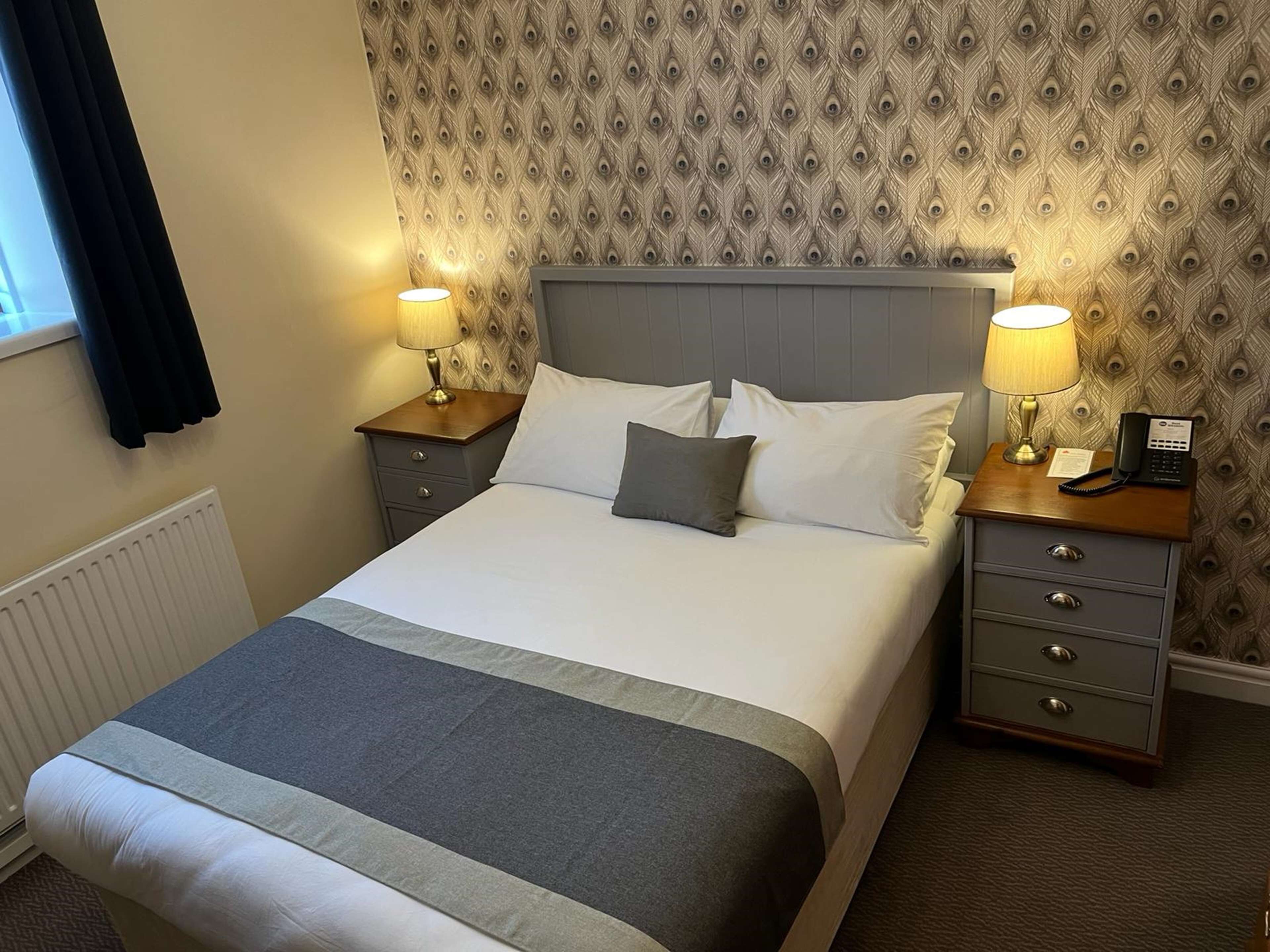 A neatly made bed with a grey and white duvet, two bedside tables with lamps, and a patterned wallpaper on the wall.