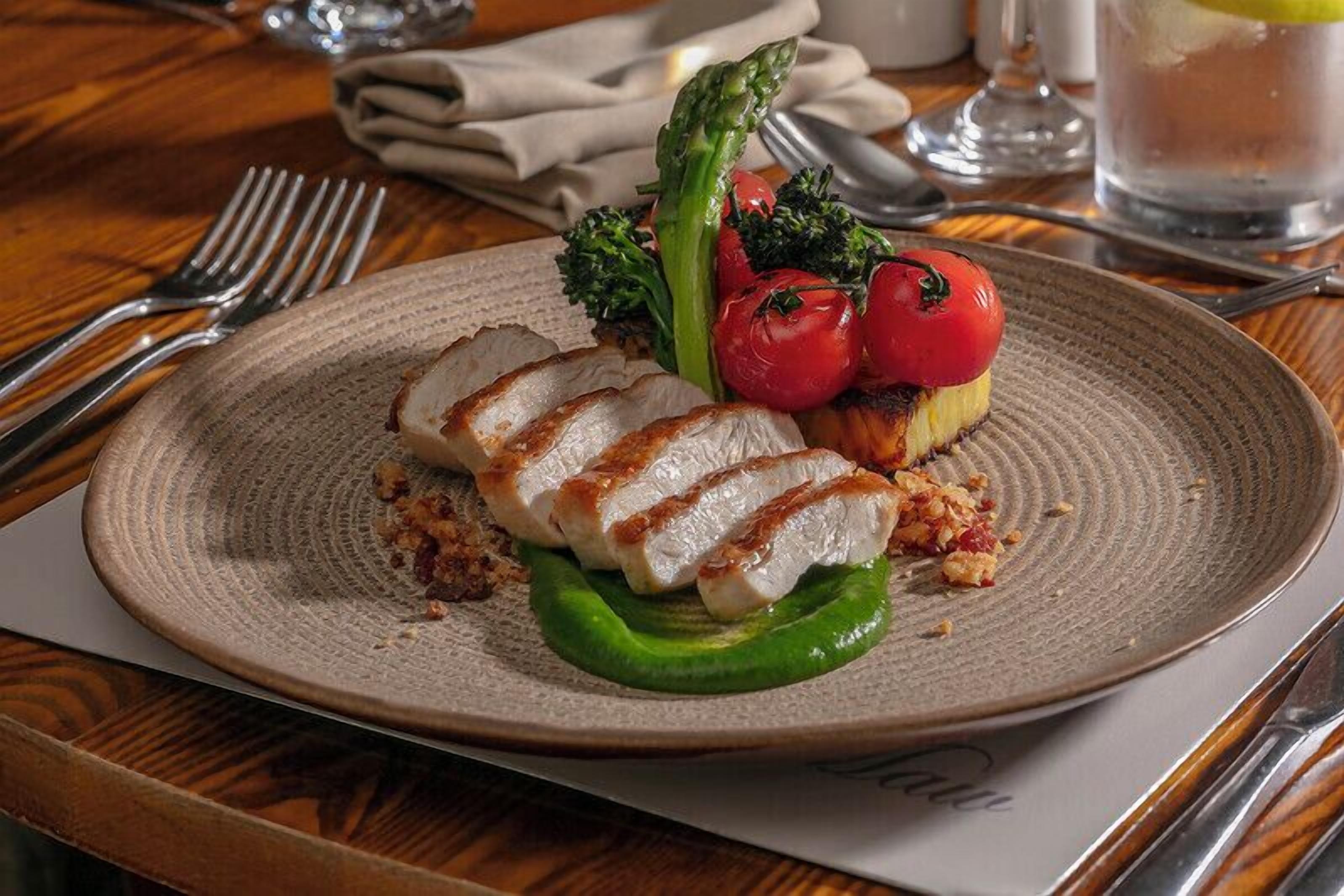 A plate of grilled chicken breast with vegetables on a textured plate.