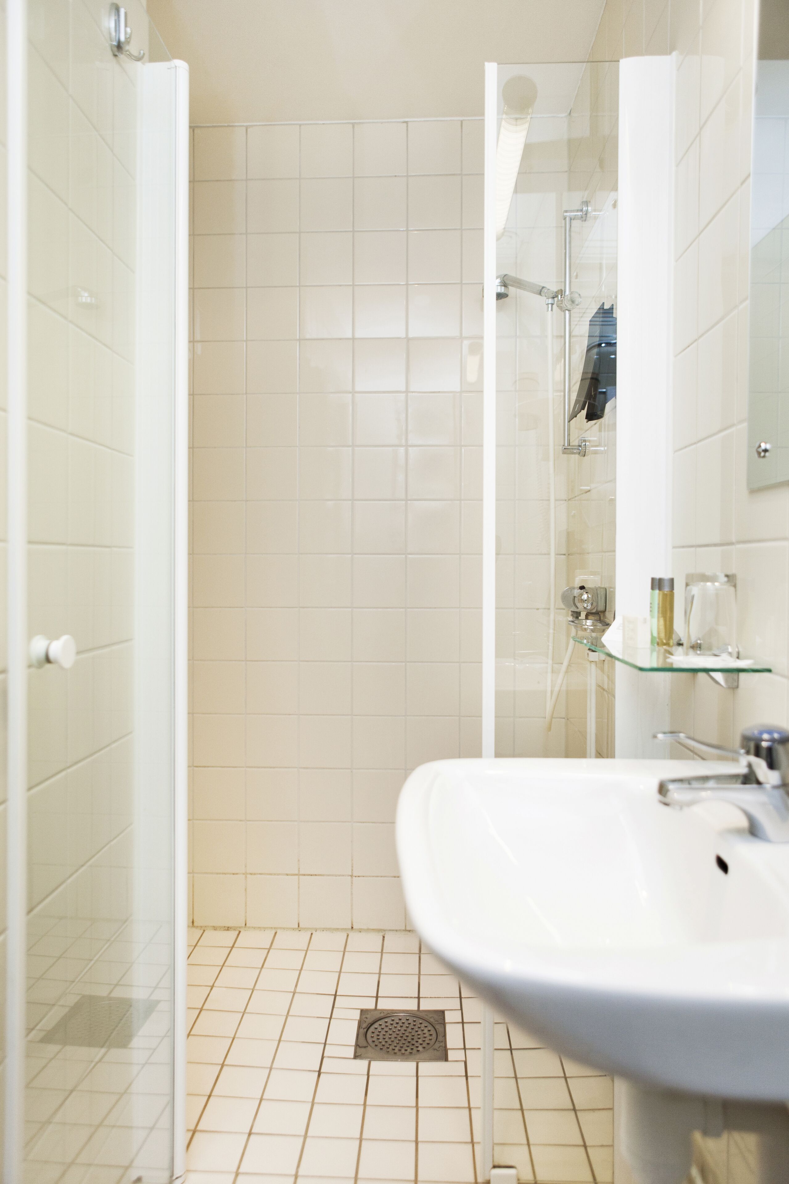 Une salle de bain avec une douche, un lavabo et une étagère en verre.