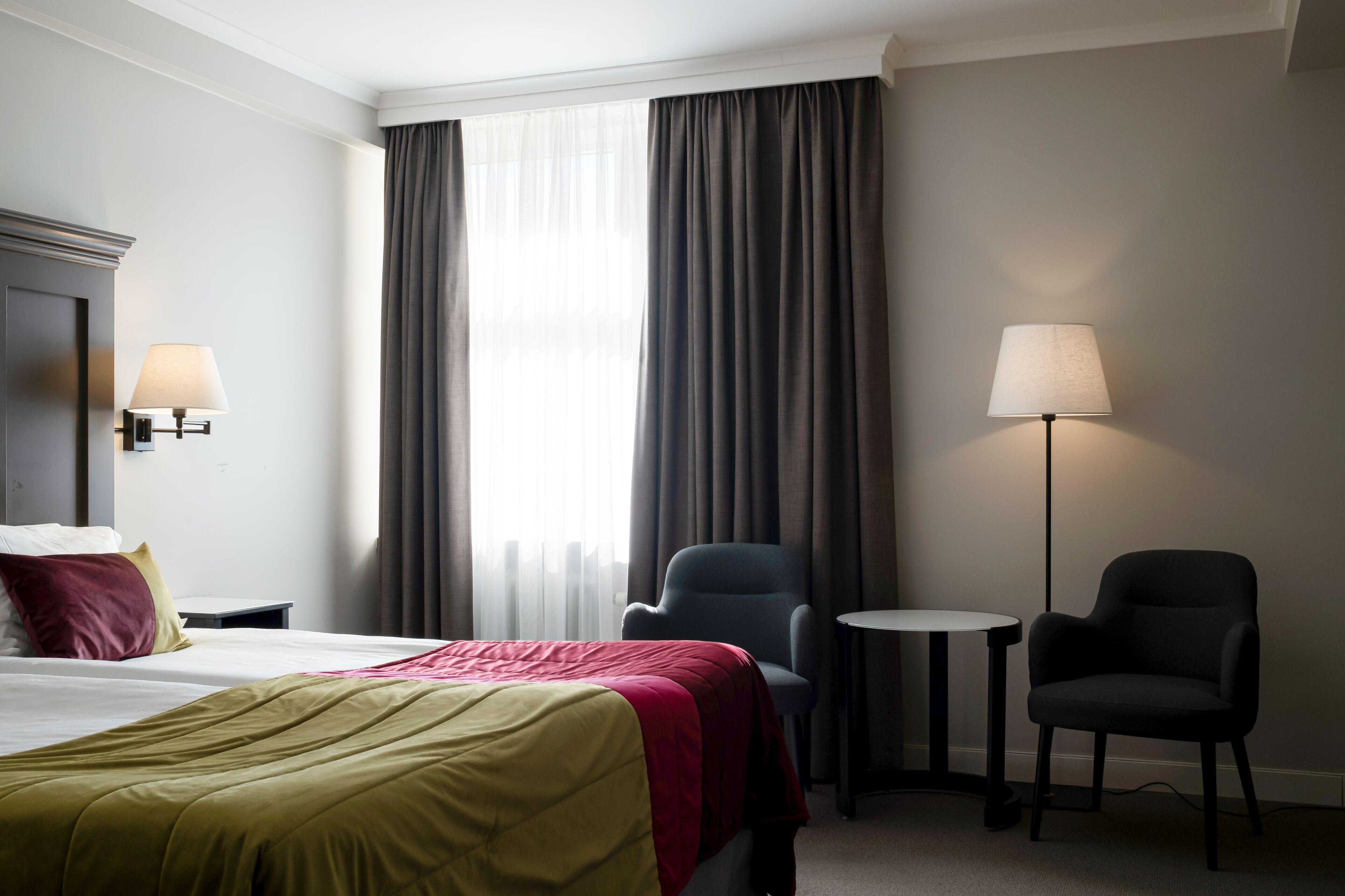 Una habitación de hotel con una cama, dos sillas, una mesita y una lámpara.