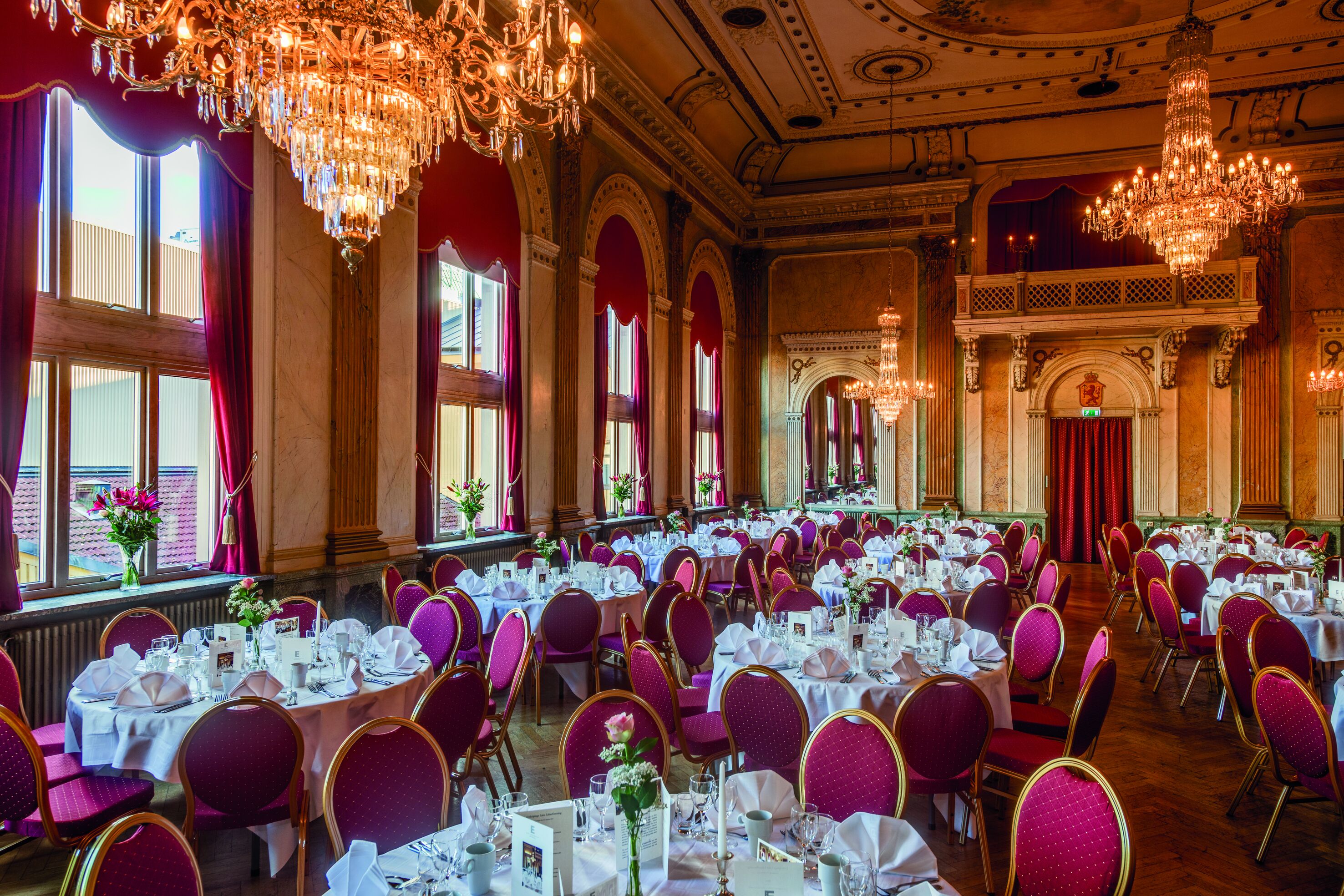 A banquet hall with round tables, purple chairs, and chandeliers.