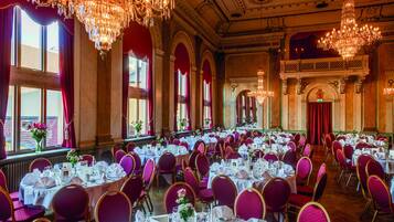 A banquet hall with round tables, purple chairs, and chandeliers.