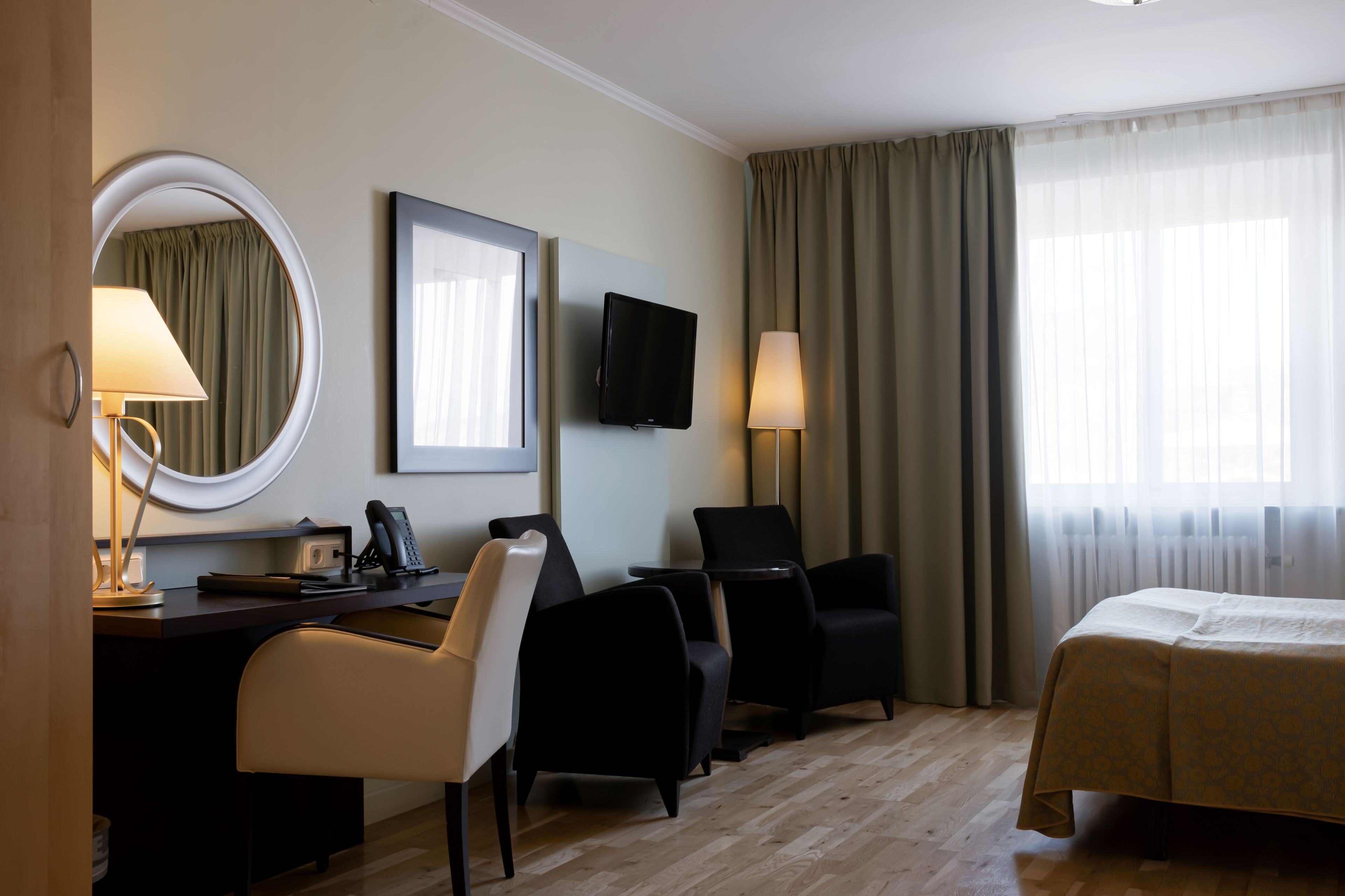 Habitación de hotel con cama, escritorio con teléfono, dos sillas, televisor y ventana con cortinas.