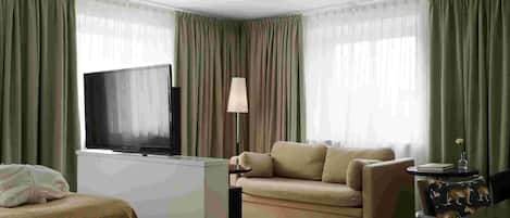 Una habitación de hotel con una televisión de pantalla plana, un sofá, una mesita y una lámpara.