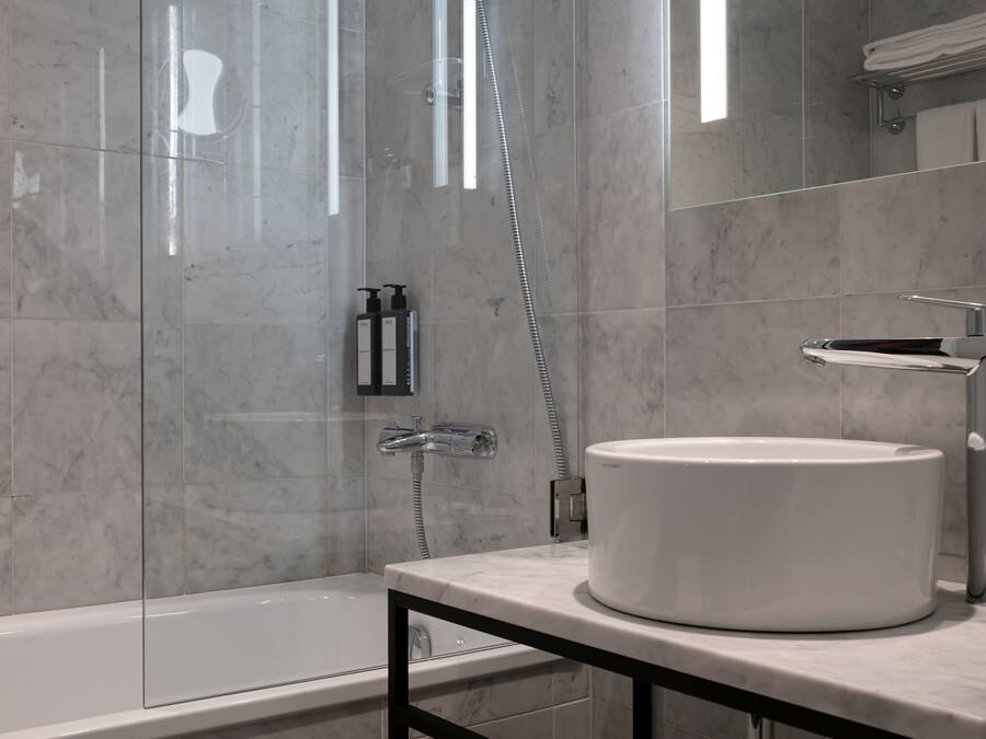 Un baño moderno con ducha envuelta en vidrio, un lavabo blanco y un revestimiento de mármol en la pared.
