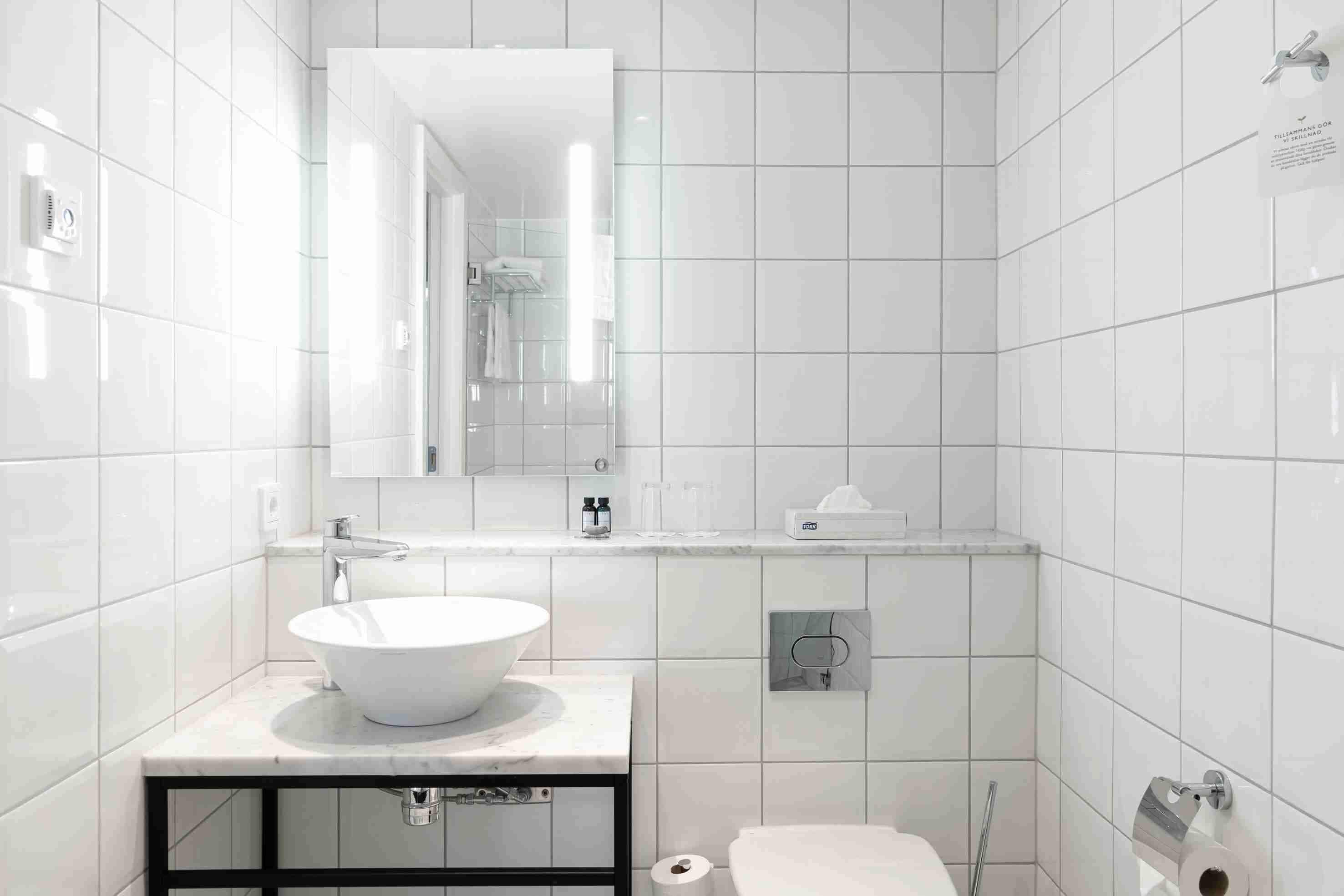 Un baño moderno con azulejos blancos, un lavabo grande, un espejo y un inodoro.